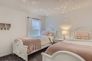 A bedroom with two beds, a nightstand, a lamp, and a ceiling with string lights.
