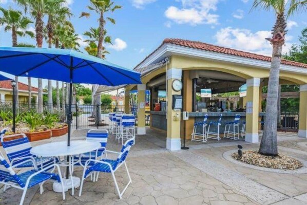 Un patio al aire libre con sillas azules, una mesa, una zona de bar cubierta y palmeras.