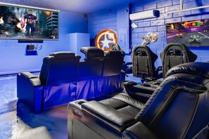Una sala de cine en casa con paredes azules, una pantalla grande y asientos de cuero negro.