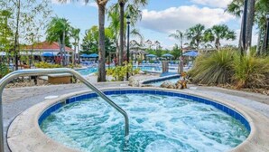 Jacuzzi con escalera metálica, rodeado de palmeras y un área de piscina con sillones de descanso.