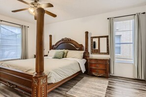 Un dormitorio con cama con dosel, mesita de noche, espejo y ventilador de techo.
