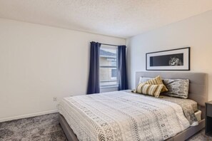 A bedroom with a bed, a window with curtains, a framed picture on the wall, and a carpeted floor. - Magical 7BR Resort Pool Home Near Disney World (Kissimmee)