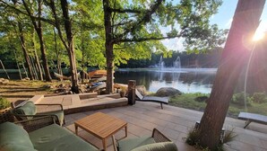 A patio area with wicker furniture, a wooden table, and a view of a pond with a fountain.