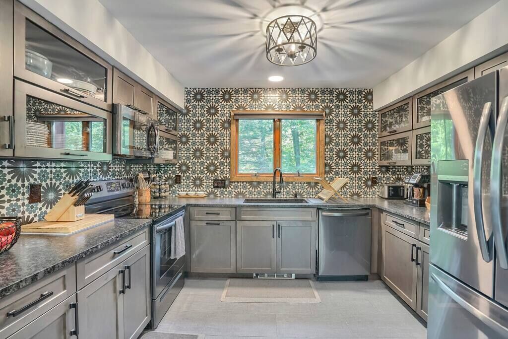Een moderne keuken met een decoratieve spatwand, roestvrijstalen apparatuur en een raam met uitzicht op bomen.