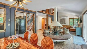 A modern living room with a wooden dining table, a central seating area with a lamp, and a staircase leading to another level.