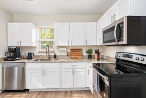 A modern kitchen with white cabinets, stainless steel appliances, a coffee maker, and a microwave. - Perfect & Cozy Home in A+ Location (Saint Petersburg)