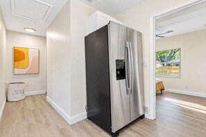 A modern kitchen with a stainless steel refrigerator, a water dispenser, and a large window with a view of greenery.