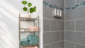 A bathroom with grey tiles, a white bathtub, and a metal towel rack with folded towels. - Perfect & Cozy Home in A+ Location (Saint Petersburg)