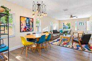 A spacious living room with a wooden dining table, colorful chairs, a sofa, and a ceiling fan. - Perfect & Cozy Home in A+ Location (Saint Petersburg)