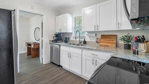 A modern kitchen with white cabinets, a stainless steel refrigerator, a coffee maker, and a wooden cutting board. - Perfect & Cozy Home in A+ Location (Saint Petersburg)