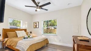A bedroom with a bed, a ceiling fan, a bedside table, a nightstand, a window, and a wooden dresser. - Perfect & Cozy Home in A+ Location (Saint Petersburg)
