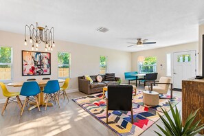 A spacious living area with a dining table, chairs, a sofa, a ceiling fan, and a large abstract painting.