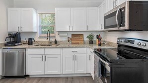 A modern kitchen with white cabinets, stainless steel appliances, and a granite countertop. - Perfect & Cozy Home in A+ Location (Saint Petersburg)
