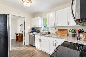 A modern kitchen with white cabinets, a granite countertop, a coffee maker, and a dishwasher. - Perfect & Cozy Home in A+ Location (Saint Petersburg)