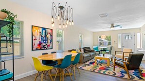 A modern living room with a wooden dining table, colorful chairs, a sofa, and a large abstract painting. - Perfect & Cozy Home in A+ Location (Saint Petersburg)