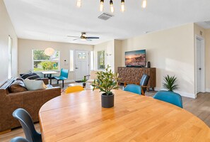 A spacious living area with a wooden dining table, blue chairs, a sofa, and a television on a wooden cabinet. - Perfect & Cozy Home in A+ Location (Saint Petersburg)