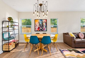 A dining area with a wooden table, blue chairs, a modern chandelier, and a colorful abstract painting on the wall.