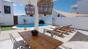 A patio with a wooden table, white chairs, and wicker hanging lamps. - Villa with private pool a stone's throw from the beach (Playa blanca)