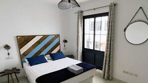 A neatly made bed with a striped headboard, a bedside table, a hanging lamp, a window with curtains, and a round mirror on the wall. - Villa with private pool a stone's throw from the beach (Playa blanca)