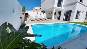 A swimming pool with lounge chairs and a white building in the background. - Villa with private pool a stone's throw from the beach (Playa blanca)