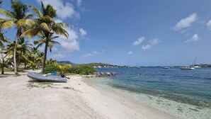 Une plage à l’eau turquoise et limpide, un bateau échoué sur le sable et des palmiers.