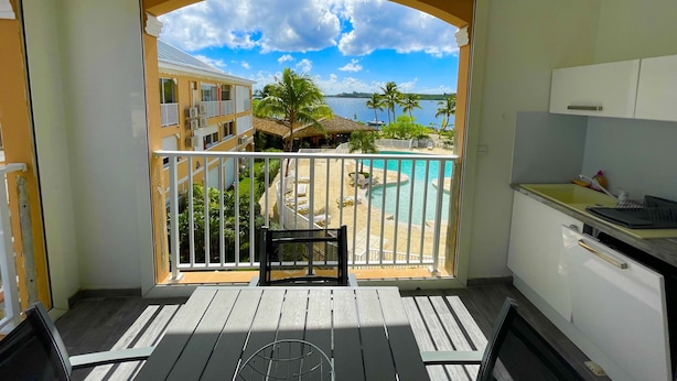 Un balcon avec vue sur une piscine, des palmiers et un bâtiment situé de l’autre côté de l’eau.