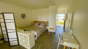 Une chambre à coucher avec un lit, un bureau et une chaise. Il y a une fenêtre qui donne sur un paysage verdoyant.