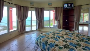Une chambre spacieuse avec un grand lit, un ventilateur de plafond et une télévision.