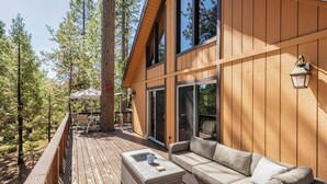 Une terrasse en bois avec un canapé et une table, entourée de grands arbres.