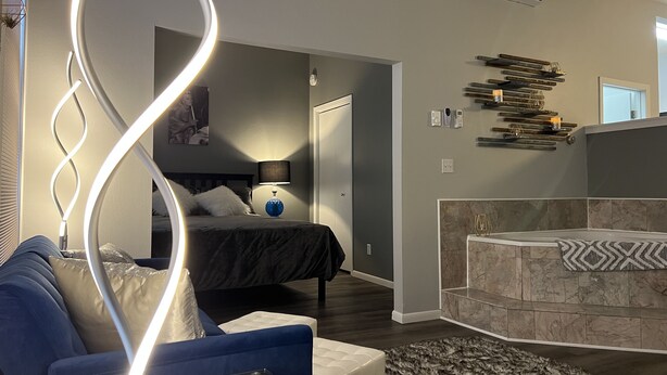 A modern living room with a blue sofa, a glass coffee table, a bed with a black headboard, and a bathroom with a marble tub. - Modern condo with jacuzzi in the heart of downtown. (Wabasha)