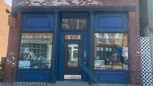A two-story brick building with a blue door and windows. The ground floor has a sign for a kayak and bike rental business, and the upper floor has a sign for tours and rentals. - Modern condo with jacuzzi in the heart of downtown. (Wabasha)
