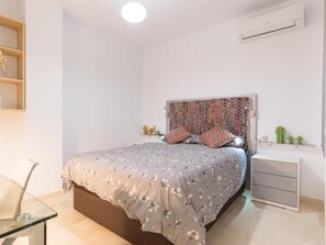 Een slaapkamer met een bed, nachtkastjes, een wandairconditioner en een plank met decoratieve spullen.