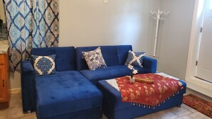 A blue sofa with patterned cushions, a small table with a red cloth, and a floor lamp. - Cosy Studio in a Private home with private entrance and door (Bronx)