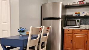 A compact kitchen with a stainless steel refrigerator, a microwave, wooden cabinets, and a blue table with two chairs. - Cosy Studio in a Private home with private entrance and door (Bronx)