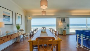 A spacious dining area with a long wooden table and chairs, large windows with a view of the beach, and a hanging light fixture. - Blue Sea Villa, Centered in La Jolla Shores! (San Diego)