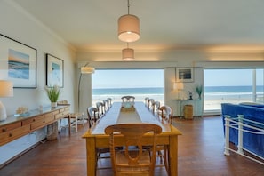 A spacious dining area with a long wooden table and chairs, large windows with a view of the beach, and a hanging light fixture. - Blue Sea Villa, Centered in La Jolla Shores! (San Diego)