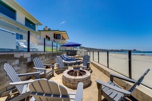 Une terrasse au bord de la plage, avec des fauteuils Adirondack, un foyer et une vue sur l’océan.
