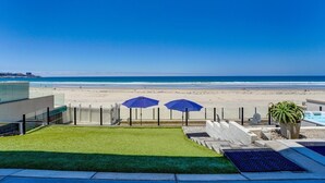 A view of a beach from a balcony with two umbrellas, a pool, and a grassy area. - Blue Sea Villa, Centered in La Jolla Shores! (San Diego)