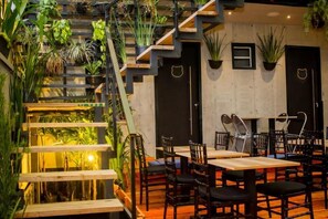 Un restaurant doté d’un escalier entouré de plantes, de tables en bois et de chaises noires.