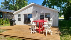 A white wooden shed with a red table and white chairs on a wooden deck. - Modern Cottage on the Water - Newly Renovated! (Dashwood)