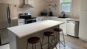 A modern kitchen with a central island, stainless steel appliances, and wooden flooring. - Modern Cottage on the Water - Newly Renovated! (Dashwood)