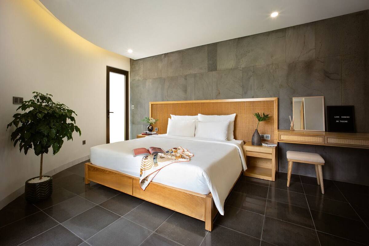 Ein modernes Schlafzimmer mit einem großen Bett, einem Nachttisch, einem kleinen Tisch, einem Sessel, einer Topfpflanze und einem wandmontierten Spiegel.
