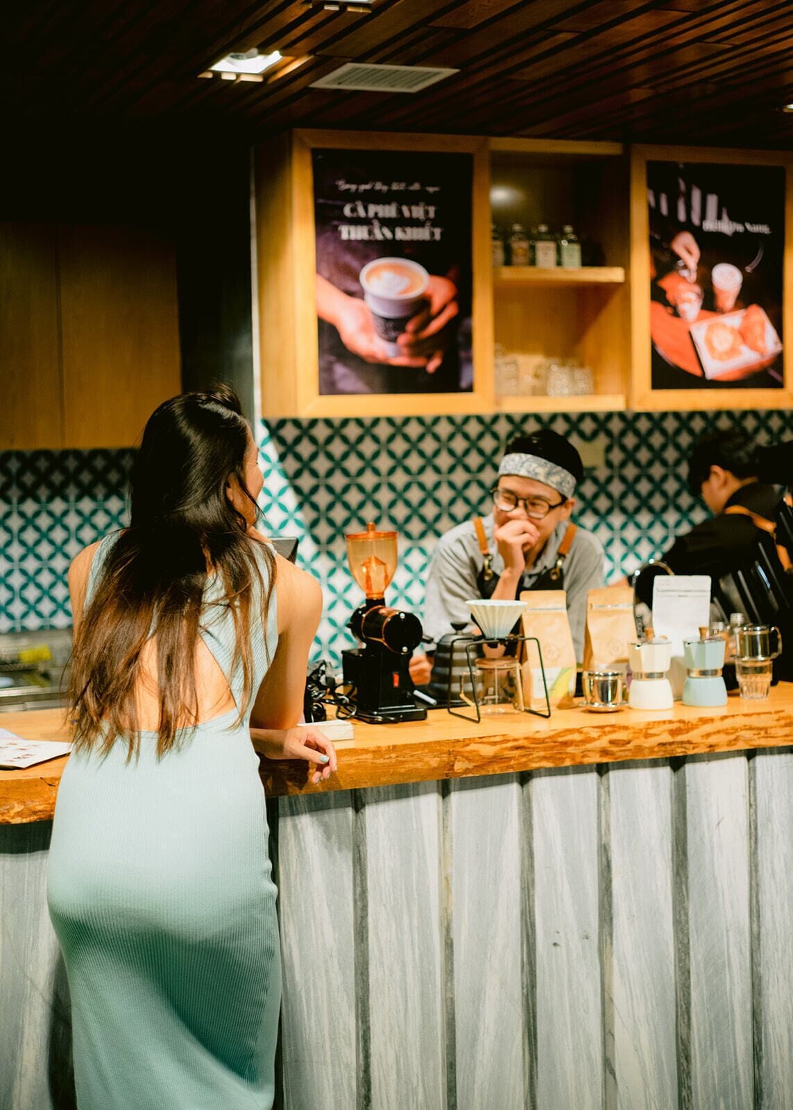 A barista preparing a drink behind a counter with a coffee machine and various coffee-making tools.