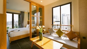 A hotel room with a bed, a sofa, a table, and a large window with a city view. - LIVIE DANANG ANTHUONG (Da Nang)