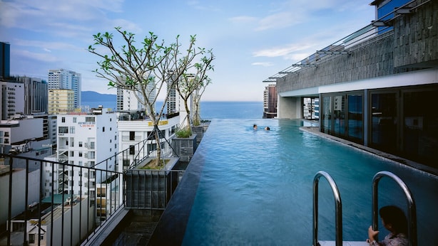 A rooftop infinity pool with a view of the ocean and cityscape, surrounded by buildings and trees. - LIVIE DANANG ANTHUONG (Da Nang)