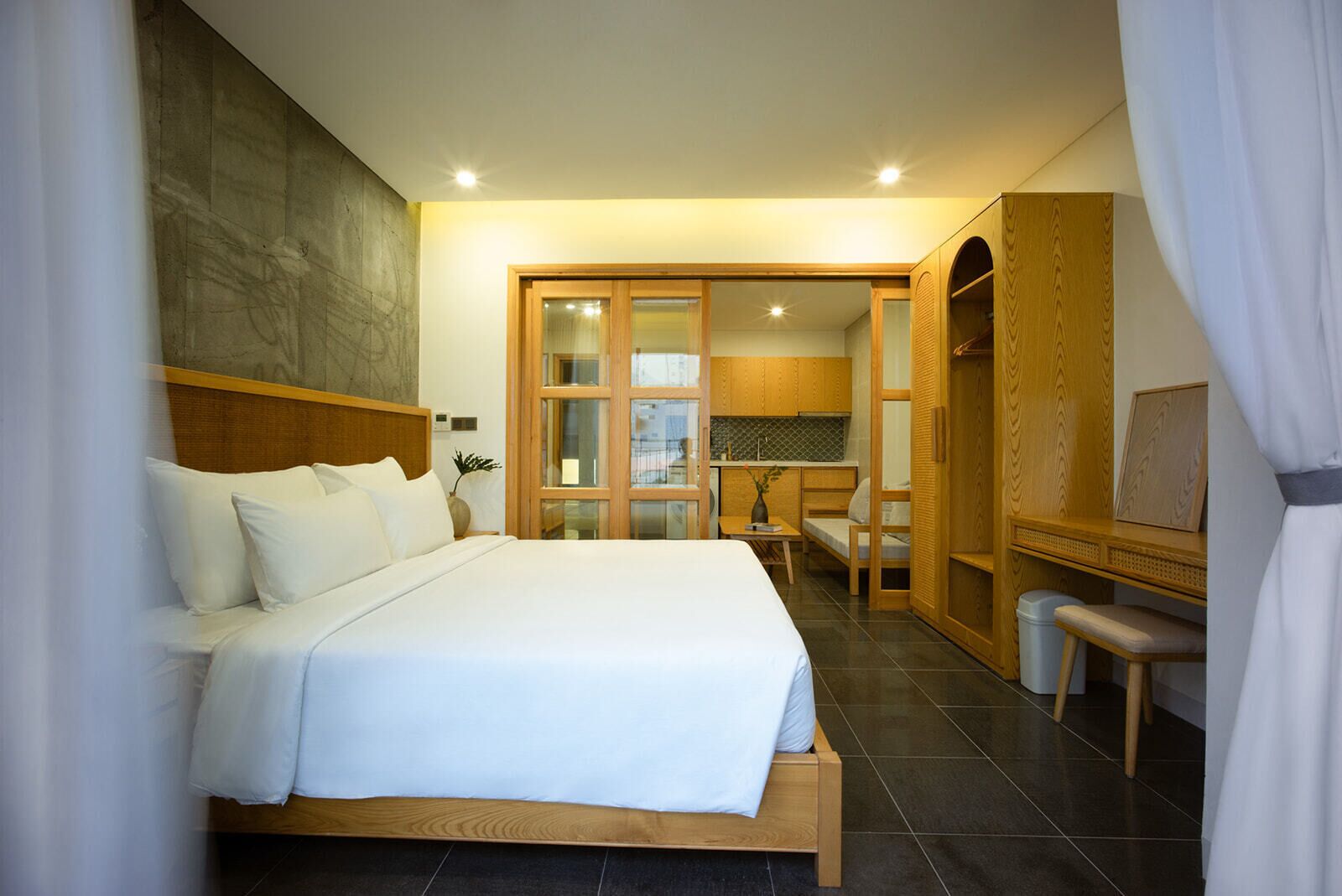 A modern hotel room with a large bed, a wooden desk, and a kitchenette.
