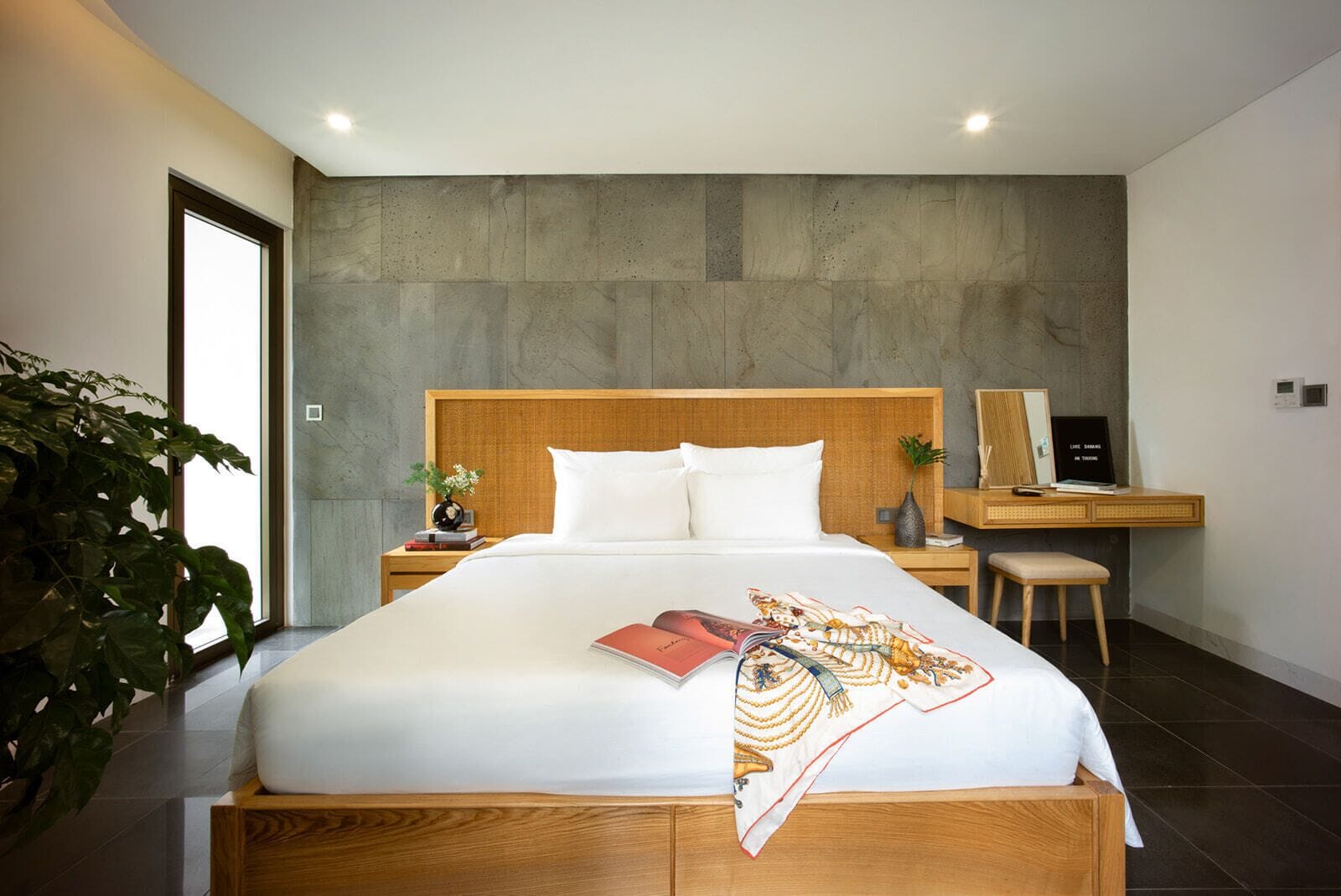 Una habitación de hotel moderna con una cama grande, un cabecero de madera, un escritorio con una silla y un ventanal amplio.