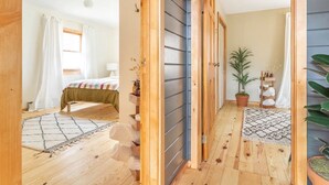 A bedroom with a bed, a bedside table, a nightstand, a window with curtains, and a wooden floor.