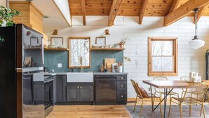 A modern kitchen with dark cabinets, a wooden ceiling, and a dining area with a table and chairs.