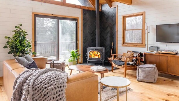 A cozy living room with a fireplace, wooden furniture, and large windows.
